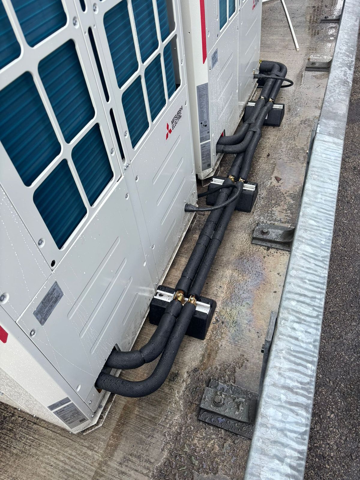 Outdoor air conditioning units in a row with insulated pipework run along the ground