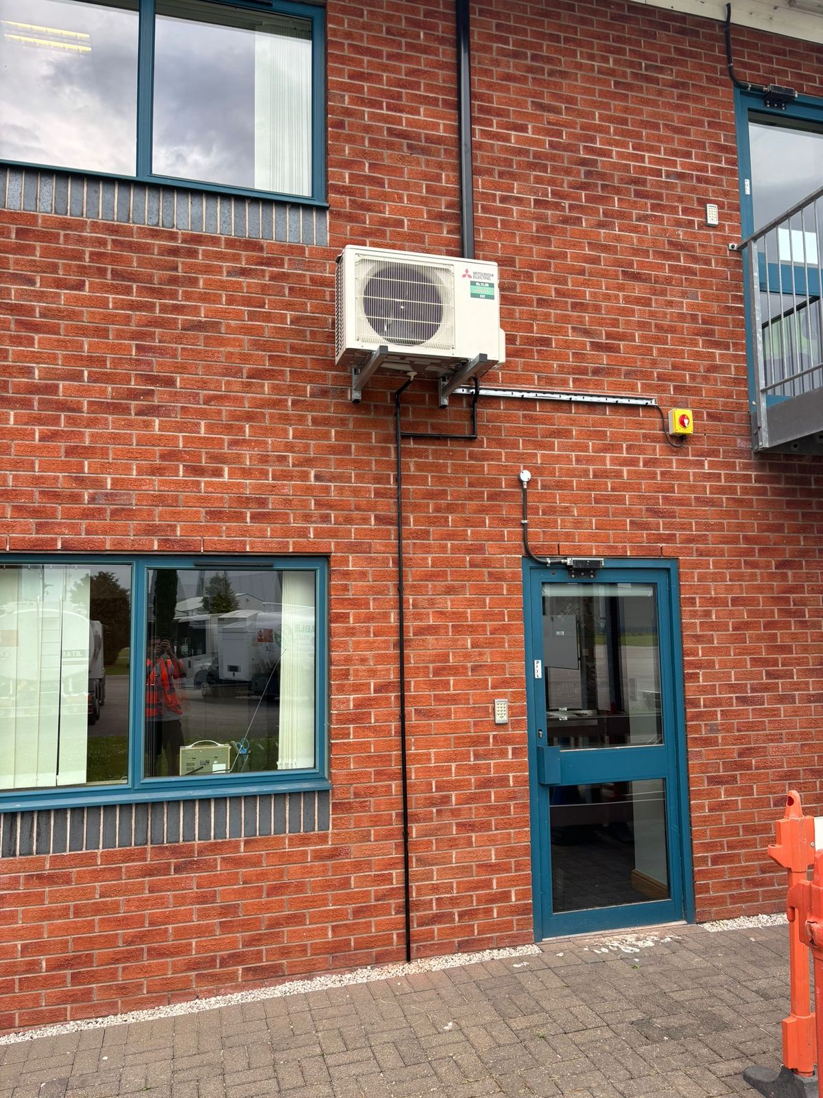 Air conditioning outdoor unit bracketed on a brick wall above a doorway