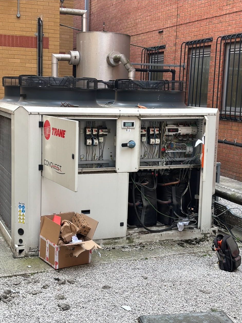 Trane packaged chiller with its control panel open on a flat roof in Salford